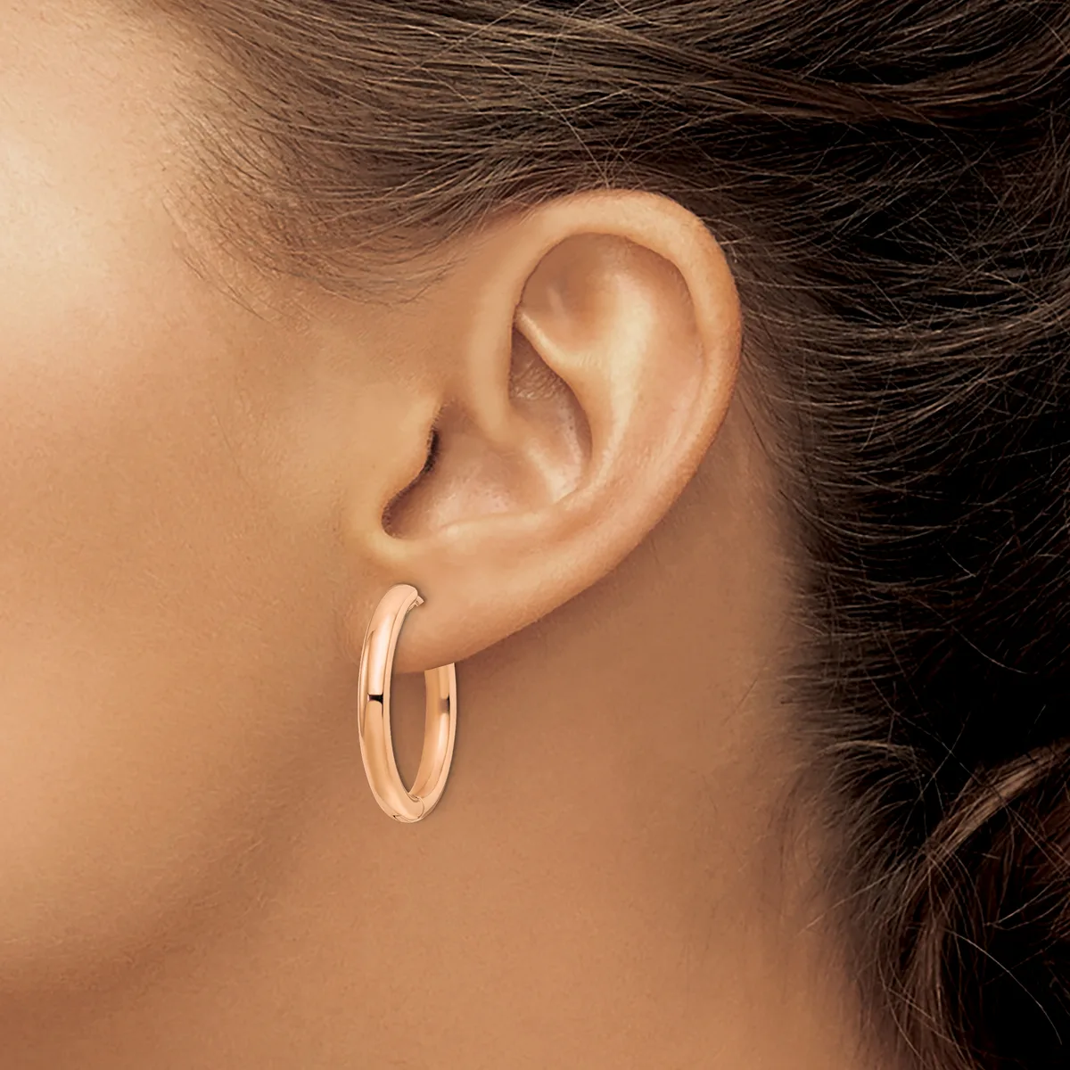 A person wearing rose gold hoop earrings with a polished finish, shown from the side profile with dark hair pulled back.