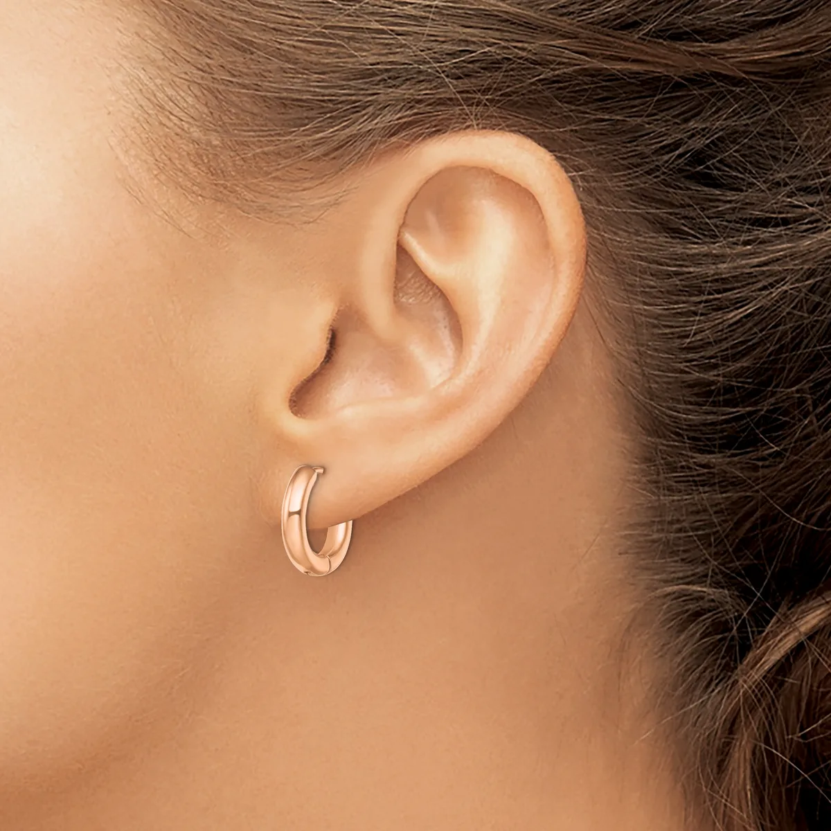 A person wearing a pair of polished silver hoop earrings with a grooved texture, shown from the side profile.