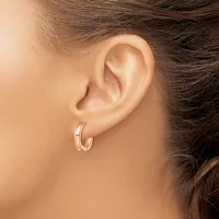 A person wearing a pair of polished silver hoop earrings with a grooved texture, shown from the side profile.