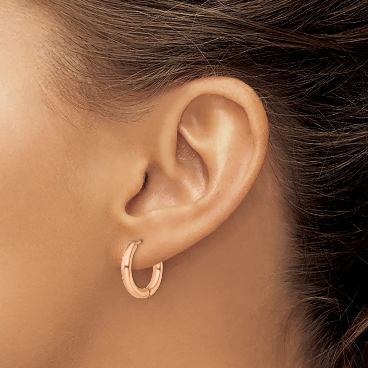 A person wearing small rose gold hoop earrings is shown from the side, displaying their ear and part of their dark hair and neck.