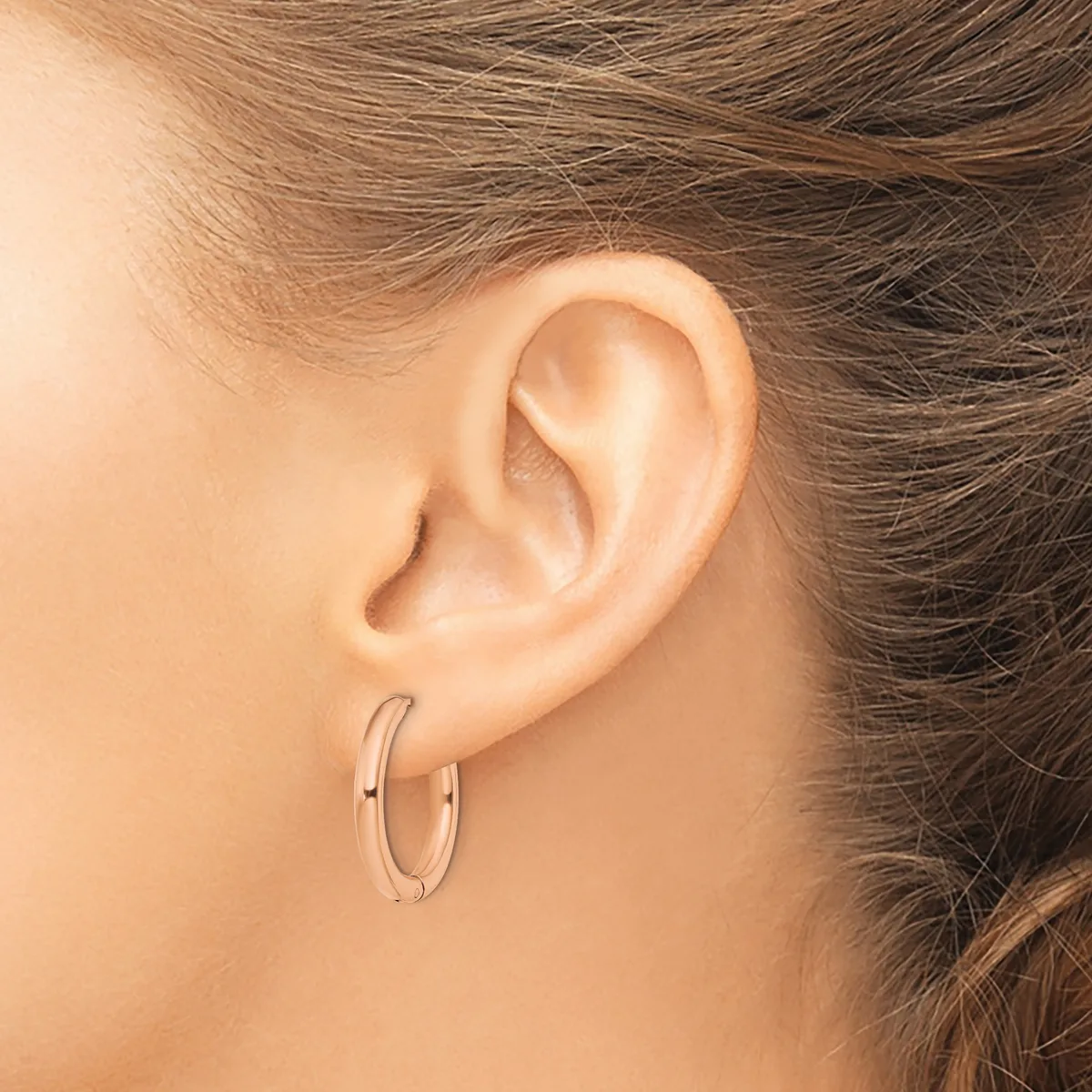 A person wearing small silver hoop earrings is shown from the side, displaying the earrings against their ear and neck with brown hair pulled back.