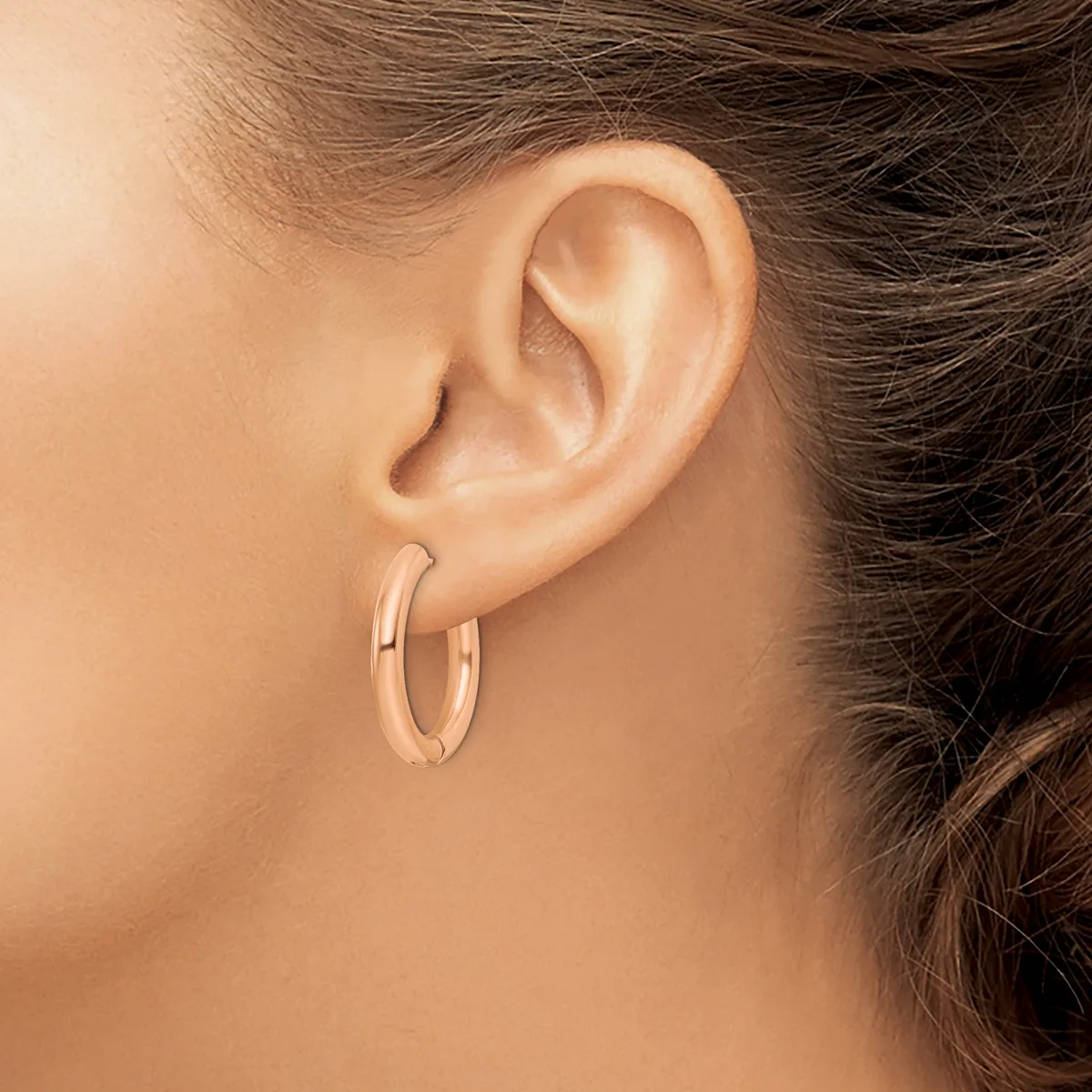 A person wearing rose gold hoop earrings shown from the side profile, displaying the ear and lower portion of brown hair pulled back.