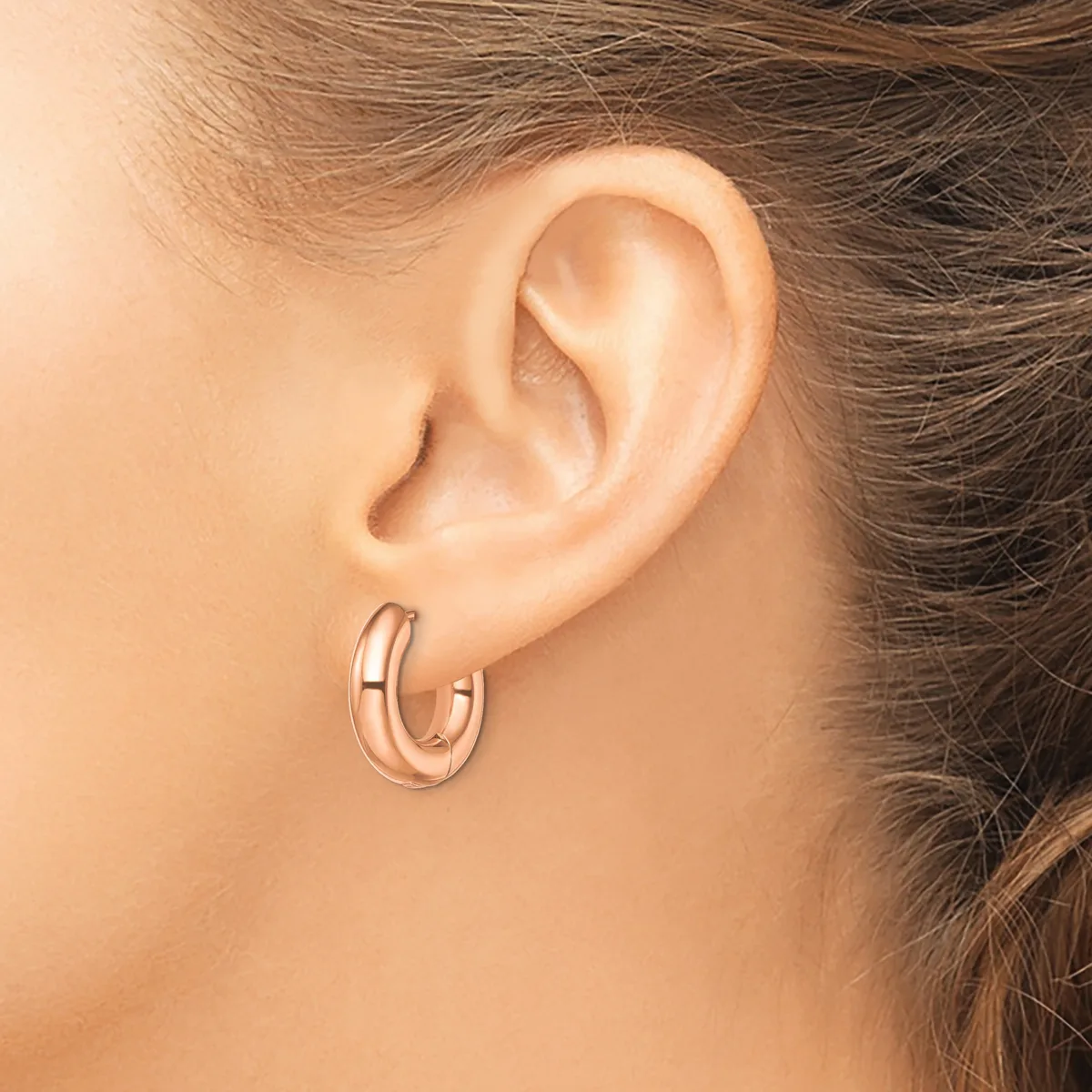 A person wearing rose gold hoop earrings with a polished finish, shown from the side profile of their ear and neck.