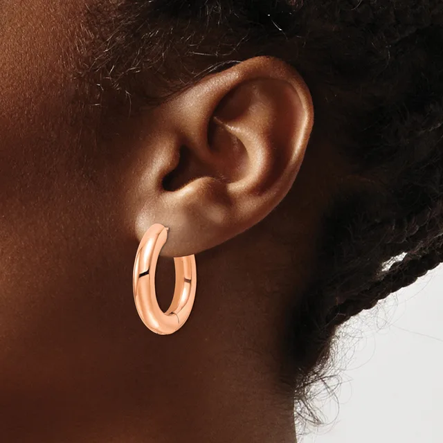 A person wearing rose gold hoop earrings with a polished finish, shown in profile against a neutral background.