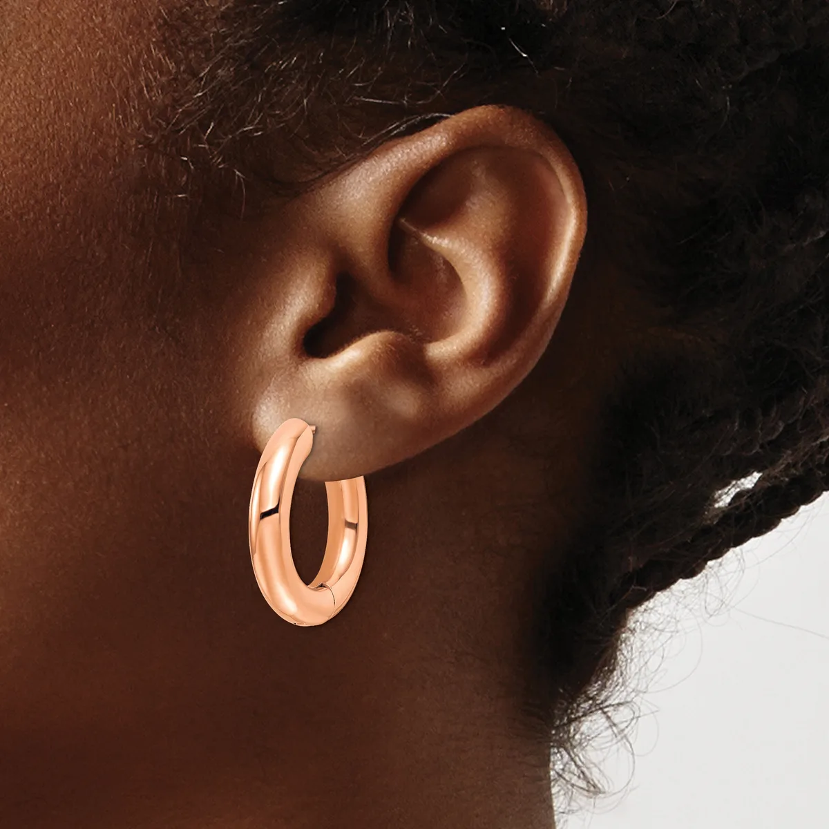 A person wearing rose gold hoop earrings with a polished finish, shown in profile against a neutral background.