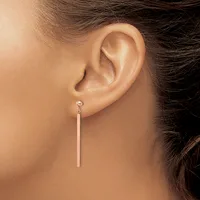 A woman wearing a long silver bar earring that hangs straight down from a stud post in her earlobe.