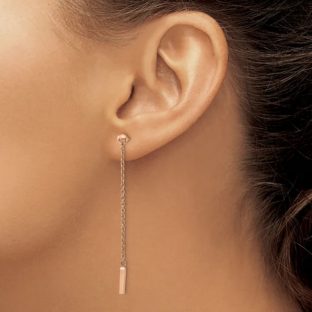 A long silver chain earring with a small rectangular pendant hangs from a pierced earlobe on a person shown in profile.