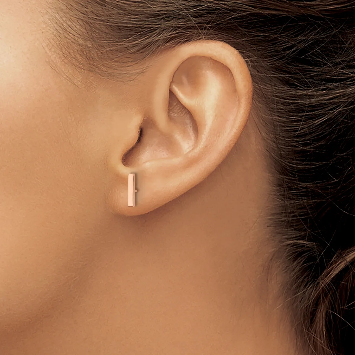 A person wearing a small rectangular gold bar stud earring in their earlobe, shown in profile view against their neck and shoulder.