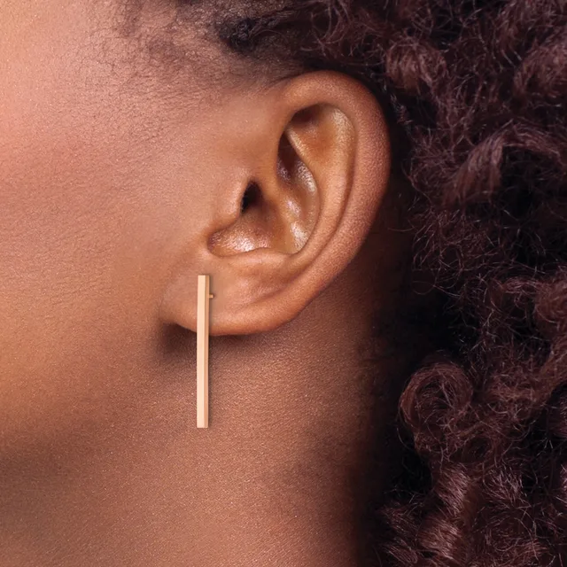 A person wearing a long, straight rectangular gold bar earring hanging from the earlobe.