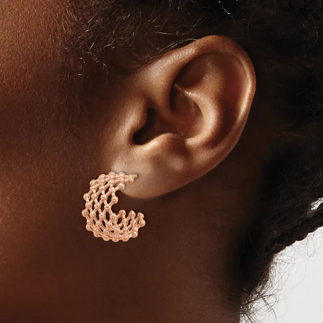 Rose gold textured chunky hoop earring worn on the earlobe of a person with brown skin and dark hair.