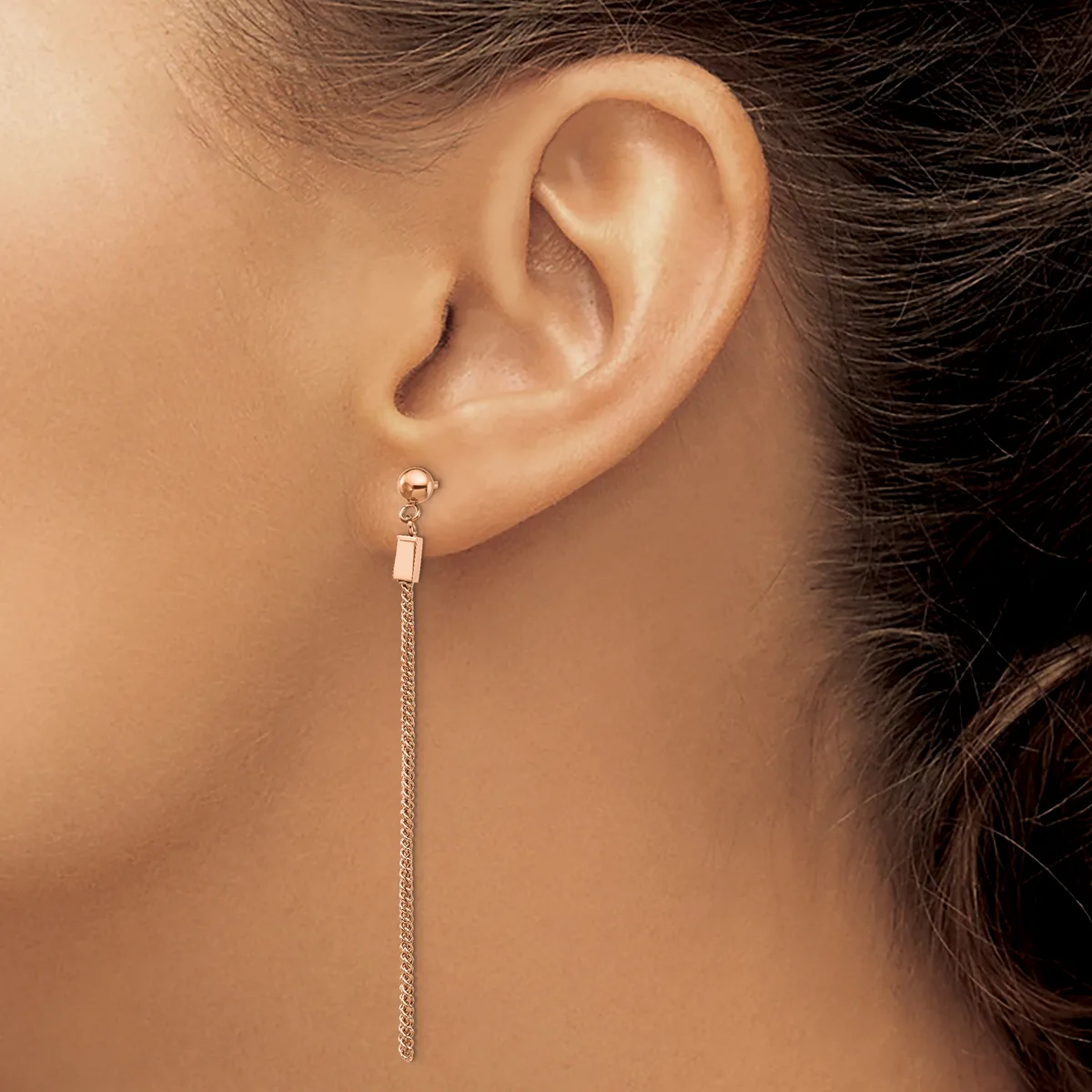A person wearing a long silver chain earring with a small rectangular connector at the top, shown from the side view of their ear and neck.