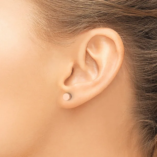 A person wearing a small round stud earring in their earlobe, shown in profile view with brown hair pulled back.