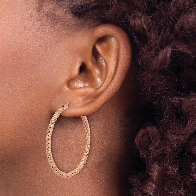Close-up side view of a person's ear wearing a textured oval hoop earring in gold-toned metal.