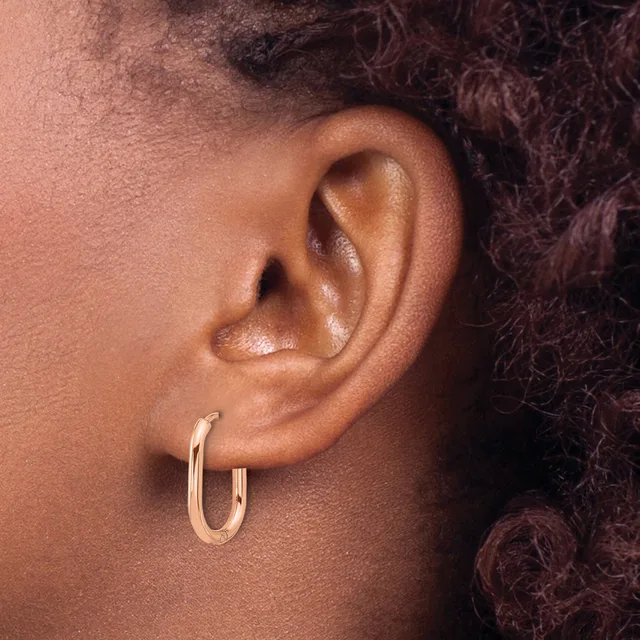 A close-up view of a person's ear wearing a pair of polished rose gold hoop earrings.