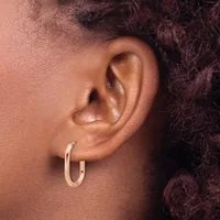 A close-up view of a person's ear wearing a pair of polished rose gold hoop earrings.