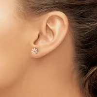 A person wearing a small flower-shaped stud earring with white petals and a center stone in their pierced earlobe.