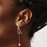 A person wearing a long chain earring with a triangular geometric top and a small rose-gold sphere hanging from the chain.