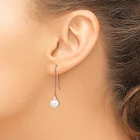 A person wearing a long silver-toned threader earring with a small pale blue spherical stone or bead hanging from the end.