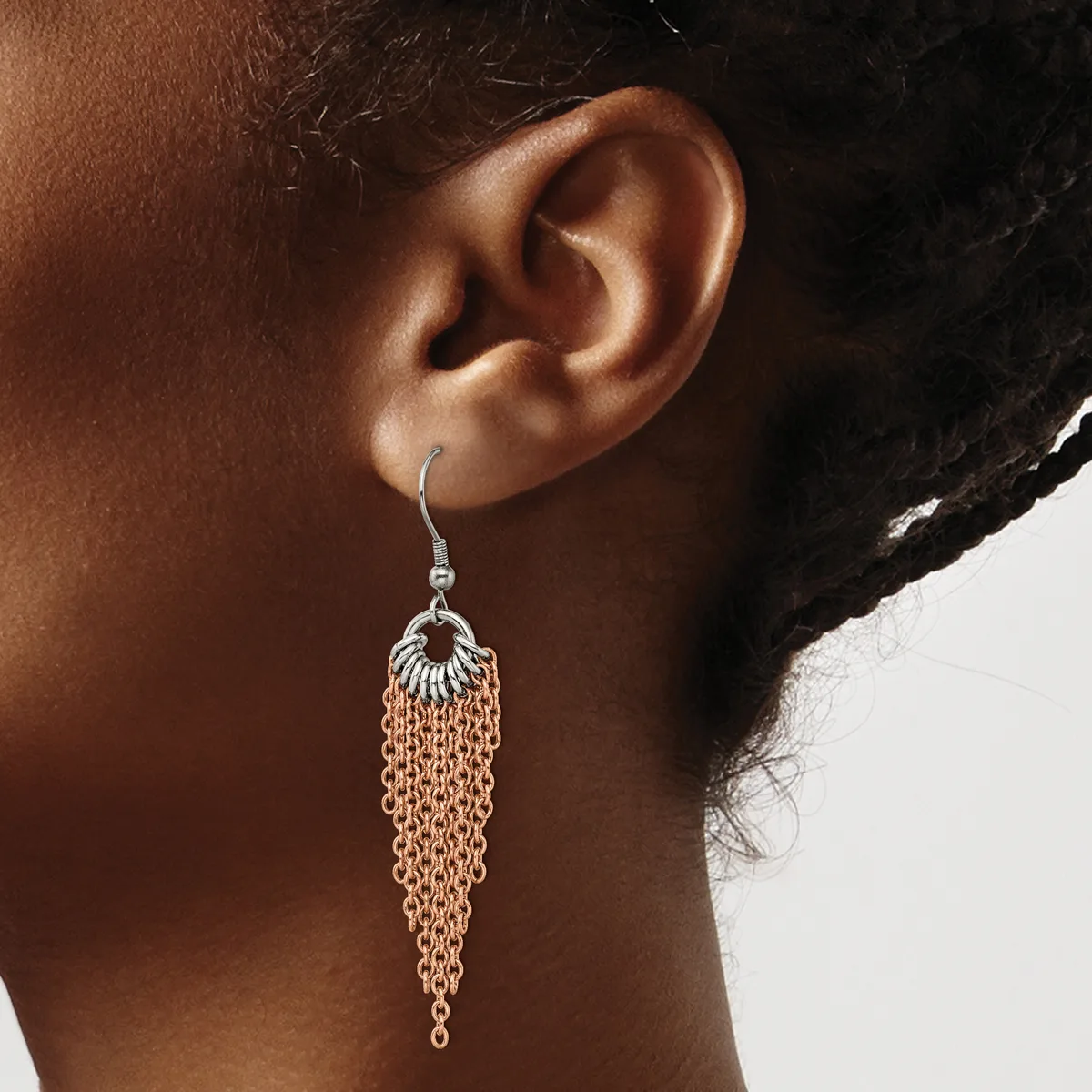 A person wearing a silver-toned chain tassel earring with a decorative top element, shown from the side view against a neutral background.