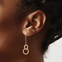 A person wearing rose gold drop earrings with two interlocking circular rings suspended from a delicate chain.