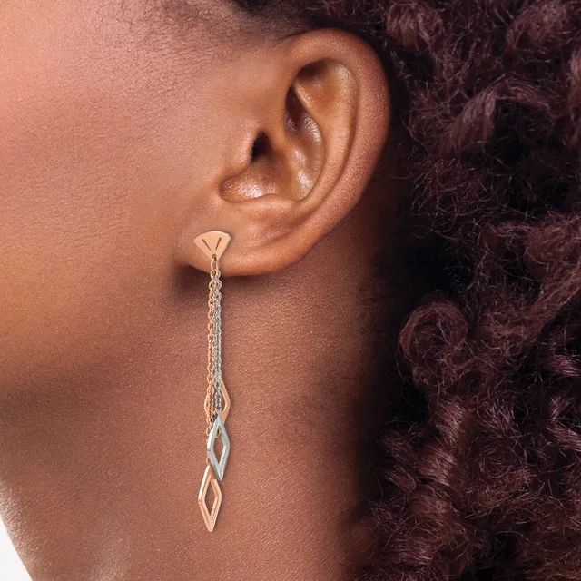 A person wearing a long silver chain dangle earring with a twisted geometric pendant, shown from the side profile against their ear.
