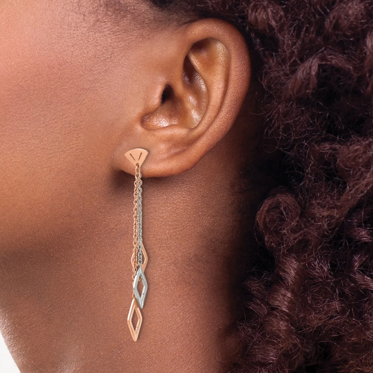 A person wearing a long silver chain dangle earring with a twisted geometric pendant, shown from the side profile against their ear.