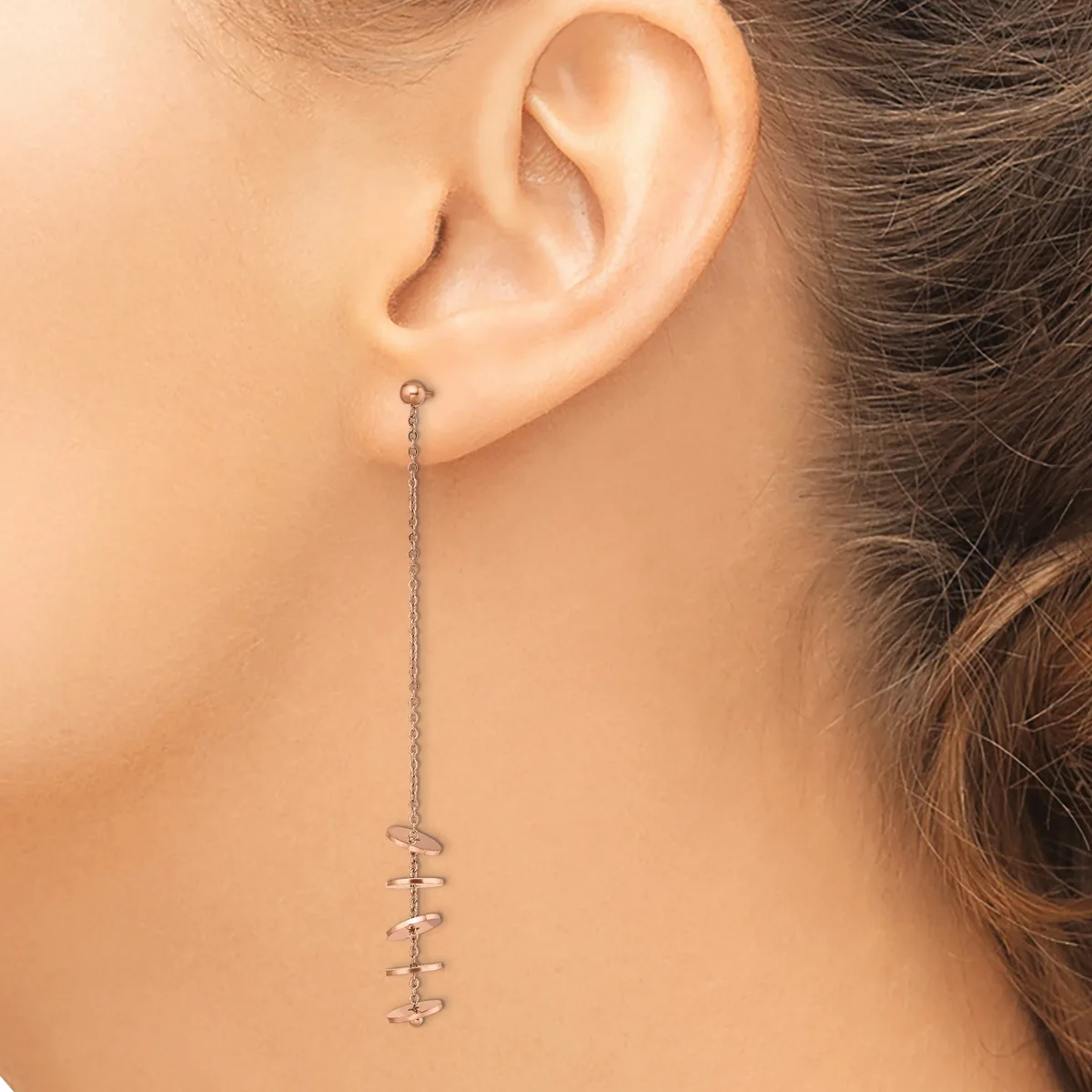 A person wearing a long silver chain earring with small spiral or coil-shaped pendants hanging from the earlobe.