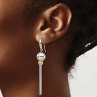 A person wearing a silver drop earring with a polished sphere at the top, a small rose gold spacer bead, and a tapered mesh chain pendant.