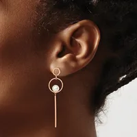 A person wearing a rose gold dangle earring with a small circular top loop, larger circular middle section with a white pearl, and a long straight bar hanging below.
