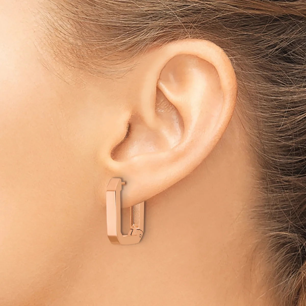 A person wearing rose gold rectangular hoop earrings with a brushed finish, shown from the side profile against their ear.