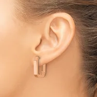A person wearing rose gold rectangular hoop earrings with a brushed finish, shown from the side profile against their ear.