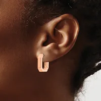 A person wearing a rose gold rectangular hoop earring with a textured surface on their earlobe.