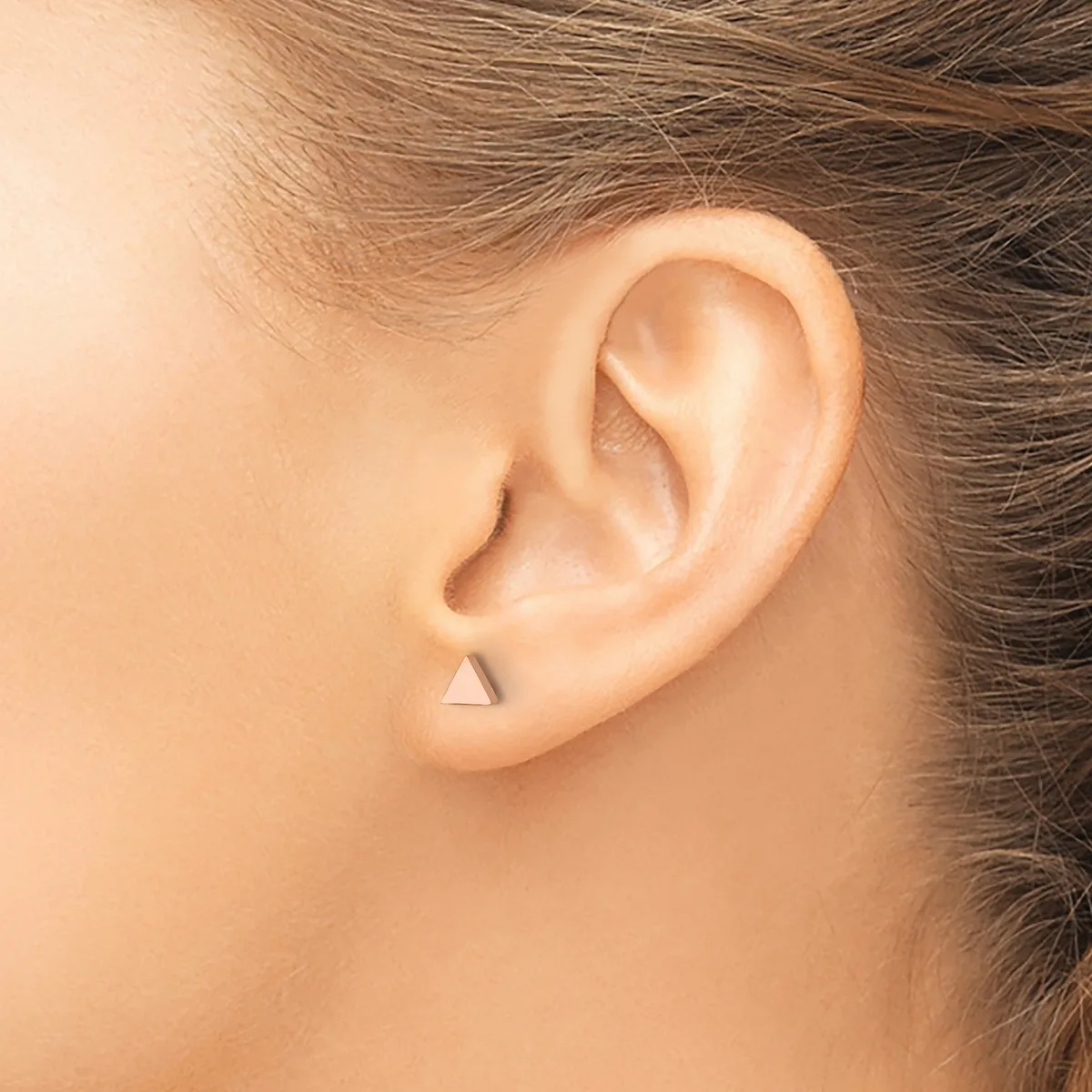 A small triangular stud earring in a polished metallic finish worn in the earlobe of a person shown in profile.