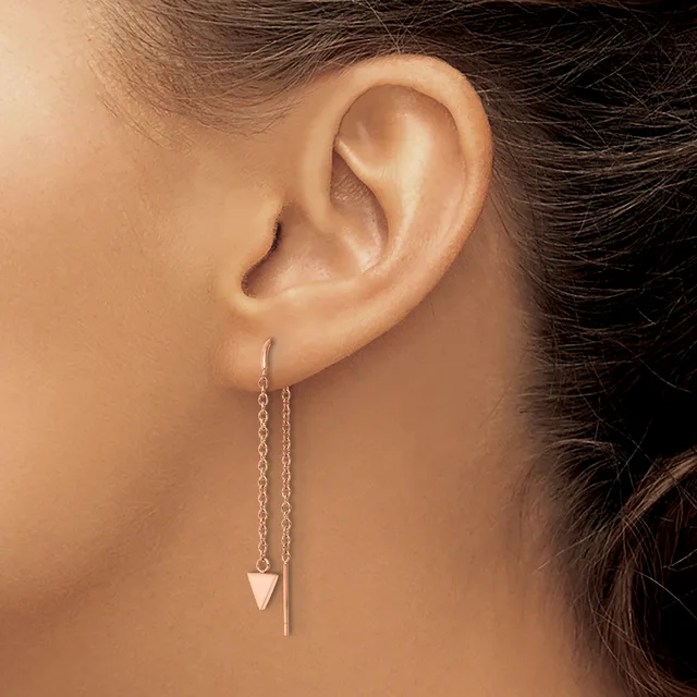 A person wearing silver threader earrings with a small triangular pendant on one ear and a chain extension on the other.