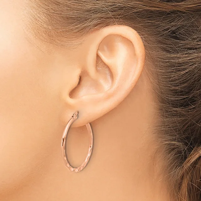 A person wearing a textured oval hoop earring in silver-toned metal, shown from the side view of their ear and neck.