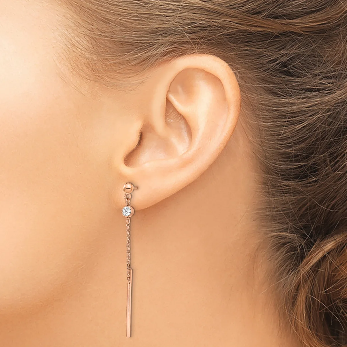 A woman's ear wearing a long silver threader earring with a small blue stone near the top and a thin chain extending down past the earlobe.