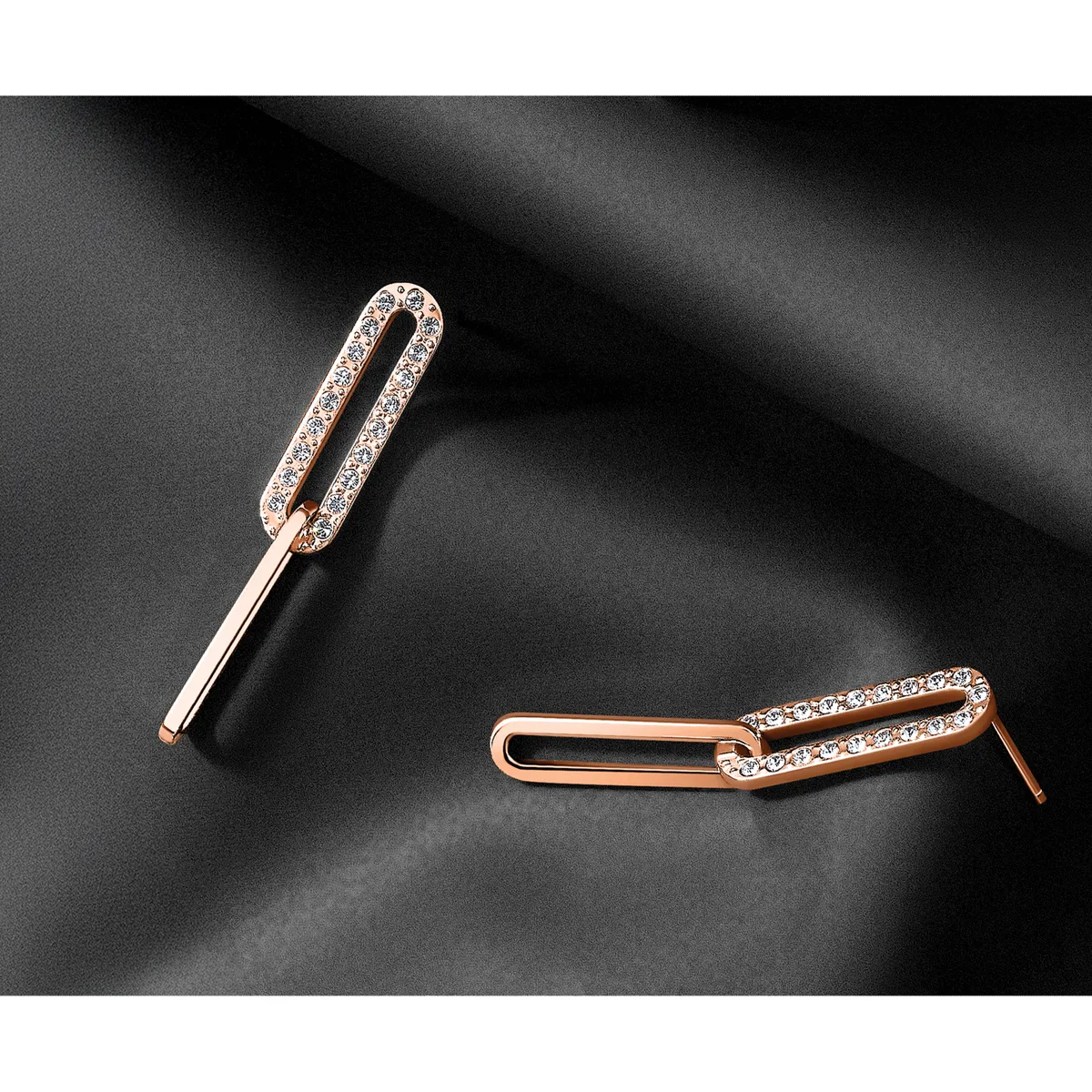 Two rose gold earrings with elongated oval shapes decorated with small crystals or rhinestones along the top edges, displayed on a dark gray surface.