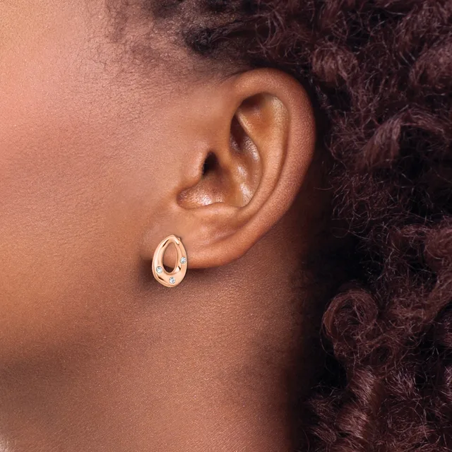 A person wearing a polished rose gold oval hoop earring, shown in profile view against their ear and dark curled hair.