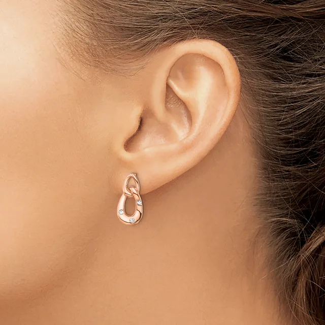 A close-up of a person's ear wearing a pair of textured silver-toned drop earrings with interlocking oval links.