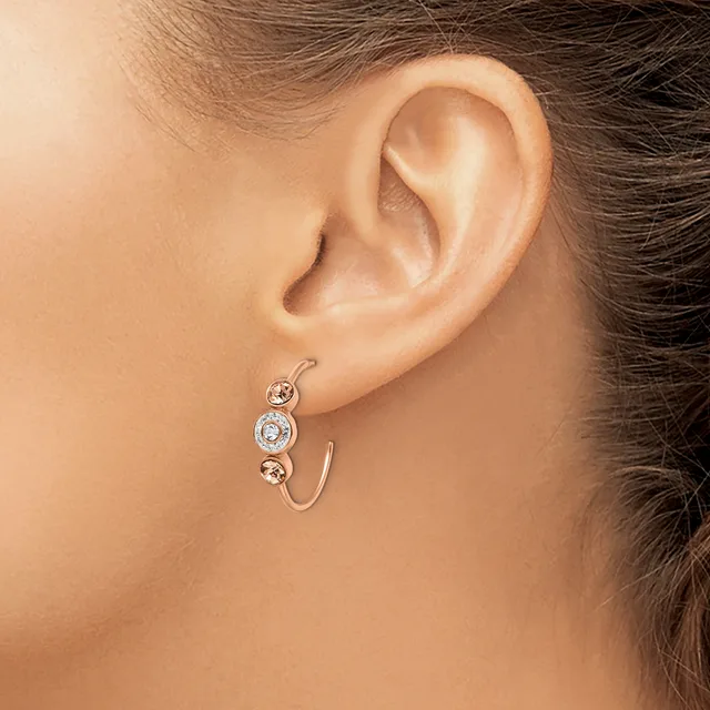 A woman wearing a curved silver hoop earring with three round gemstones in graduated sizes set along the front.