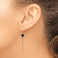 A person wearing a long silver drop earring with a small black spherical bead at the top and a thin metal bar extending downward.