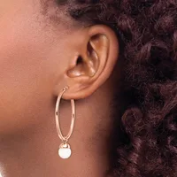 A person wearing a rose gold hoop earring with a small white circular pendant hanging from it.