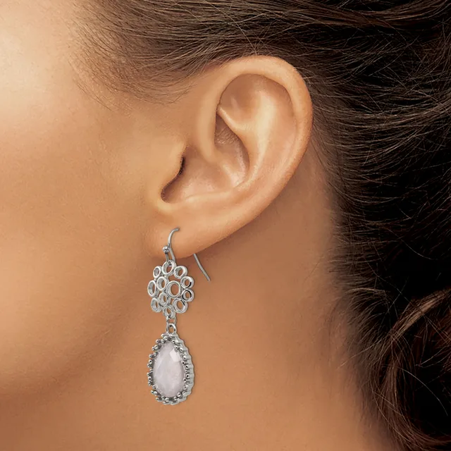 A woman wearing a silver teardrop pendant earring with a white stone surrounded by a decorative openwork circular top piece.