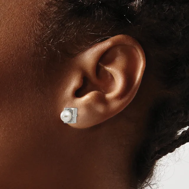 A square silver stud earring with a white pearl sits on the earlobe of a person shown in profile.