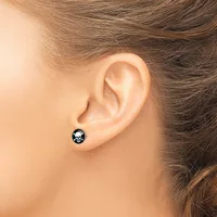 A person wearing a small round black stud earring with a white skull and crossbones design in the earlobe.