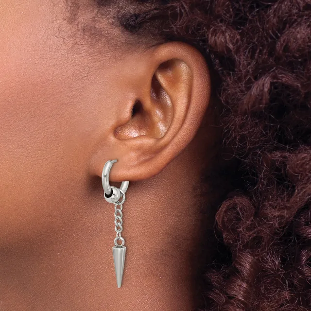 A person wearing a silver hoop earring with a dangling spike pendant in their pierced earlobe.