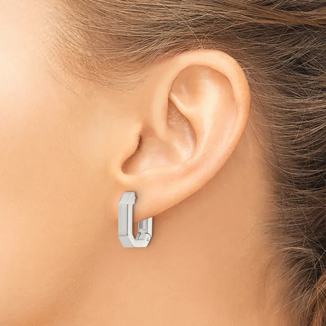 A person wearing a pair of small rectangular silver-toned hoop earrings with a polished finish, shown from the side view of their ear.