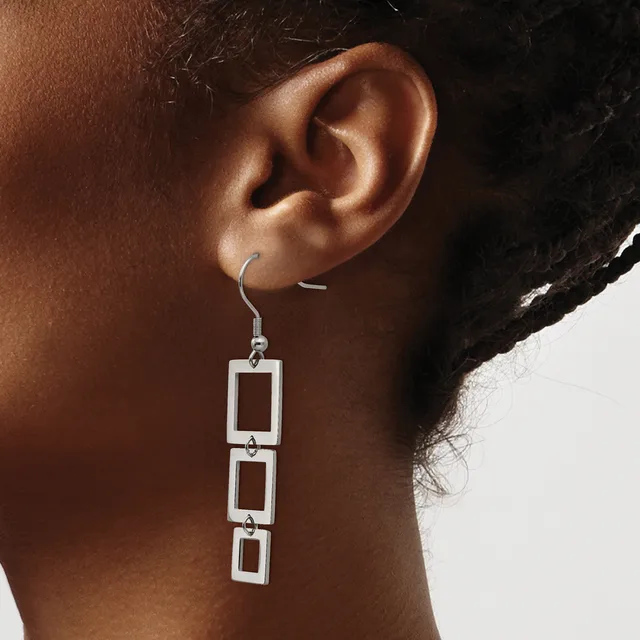 A person wearing silver-toned drop earrings made of three connected rectangular frames hanging from a hook-style ear wire.