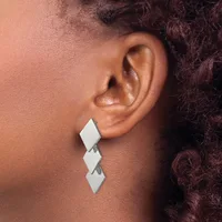 A person wearing a white three-part diamond-shaped dangling earring on their earlobe, shown in profile against their neck and shoulder.