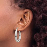A person wearing a polished silver oval hoop earring in their earlobe, shown in profile against their shoulder and dark curly hair.